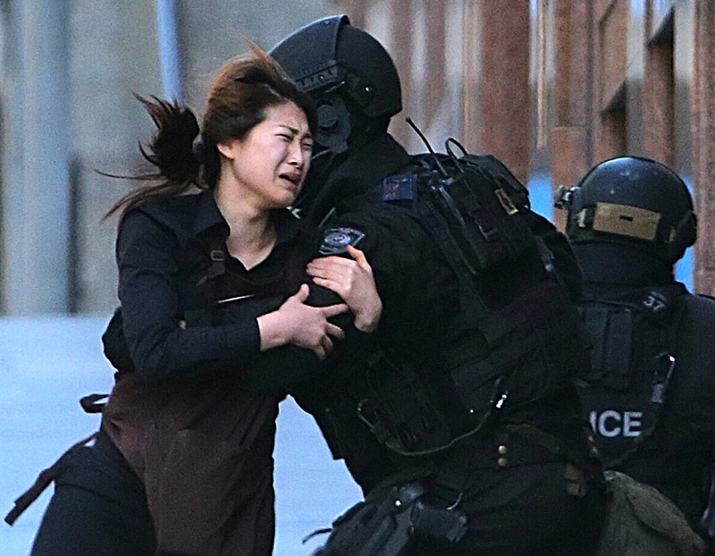 A hostage runs to an armed tactical response police officers for safety after she escaped from a cafe under siege at Martin Place in the central business district of Sydney, Australia.