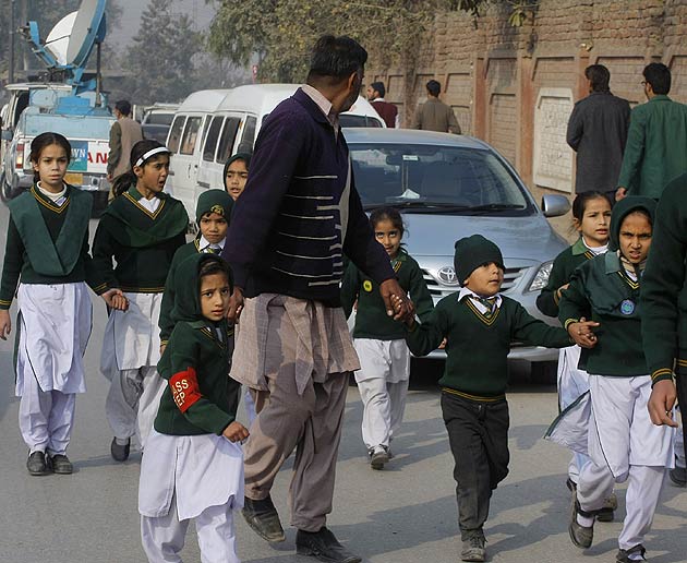 A security officer escorts shepherds students rescued from nearby school during a Taliban attack in Peshawar, Pakistan. (AP)
