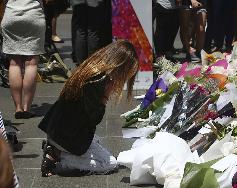A woman kneels down as she lays flowers in a makeshift memorial near the site where a gunman held hostages. AP