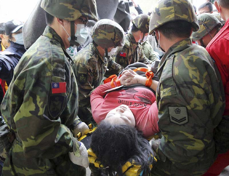 Earthquake in Taiwan: Local media said the building included a care center for newborns and mothers, and a newborn was among the dead in the disaster. The high-rise building "first starting shaking horizontally, then up and down, then a big shake right to left,'' said Tainan resident Lin Bao-gui, a secondhand car salesman whose cars were smashed when the building collapsed across the street from him. “I stayed in my bed but jumped up when I heard the big bang that was the sound of the building falling,'' he said. <br>Image Caption: A woman is rescued from a collapsed building after an early morning earthquake in Tainan, Taiwan(AP)</br>