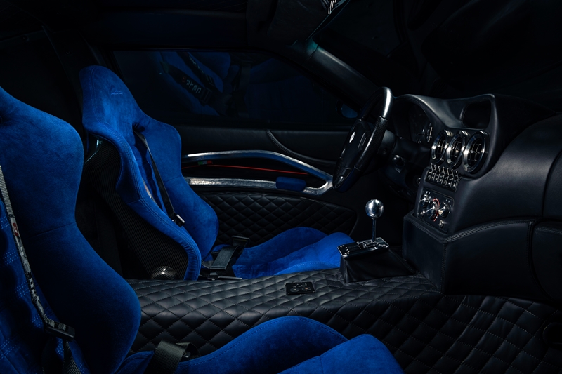 The Breadvan Hommage features a handmade interior. The iconic outline of the exterior design has been embroidered into the blue Alcantara carbon fibre backed seats. The monogram can also be found on the dials, all 7 boasting pure silver inlays. The clock says: ‘che importa’. Italian for ‘who cares!’ All switchgear is made out of milled aluminium, linking to the gated shifter, which is set on a raised block. The driver is surrounded by quilted black leather: it can be found on the centre console, the lower door cards and the headliner. The door panels feature an unpainted, hand beaten aluminium element, which links to the custom body, made in the exact same way. A small embroidered Italian flag in the corner of the aluminium insert is highlighting the roots of the vehicle. The door is opened through pulling a lightweight red cord, whilst a blue Alcantara insert functions as a grab handle to close it.
