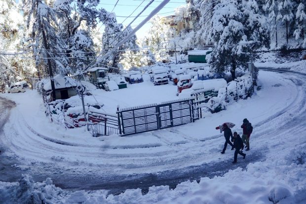 People walk on a snow covered road after heavy snowfall in Shimla. (PTI Photo)