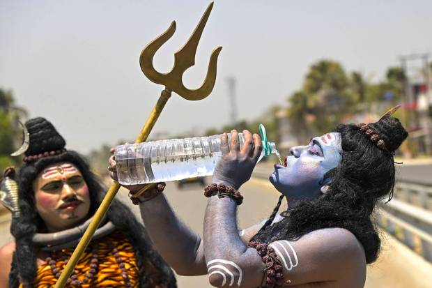 A folk artist dressed as Lord Shiva quenches his thirst during a hot summer day, in Nadia. (PTI)
