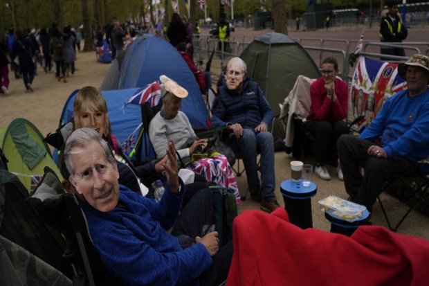Royal fans wearing masks of members of the British Royal family including King Charles III, left, sit in their place as they queue along the Mall, part of the Coronation route in London on Friday. (Photo: AP)