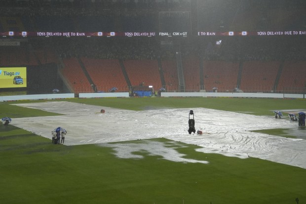 Groundsmen hold umbrellas near the covered pitch as it rains ahead of the IPL 2023 final cricket match between Gujarat Titans and Mumbai Indians at the Narendra Modi Stadium, in Ahmedabad. (Image/PTI)