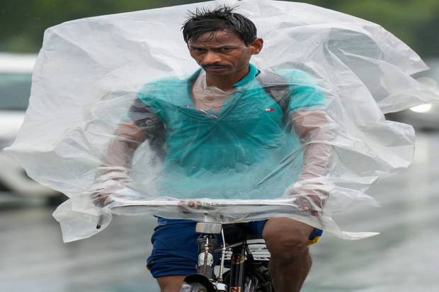 New Delhi: A commuter wrapped in a plastic sheet to protect himself from rains pedals his bicycle to workplace, in New Delhi. (PTI Photo)