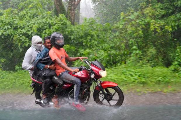 Three men ride on a motorcycle under the rain in Kotdwar district of Uttarakhand. (AP Photo)