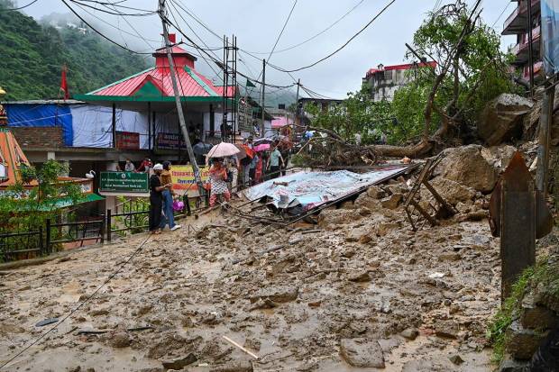 Commuters walk by the debris that has blocked the Chandigarh-Manali highway after a landslide, near Mandi. (PTI Photo)