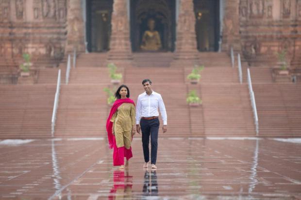 Despite the heavy rainfall, Rishi Sunak and wife Akshata Murthy made their way to the temple at 6:30 am, where they were led through the temple grounds by the guidance of temple priests. (Image/Reuters)