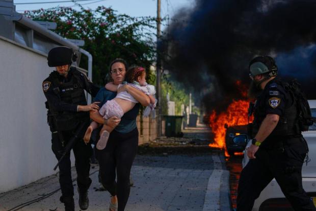 Police officers evacuate a woman and a child from a site hit by a rocket fired from the Gaza Strip, in Ashkelon, southern Israel. (Image/AP)