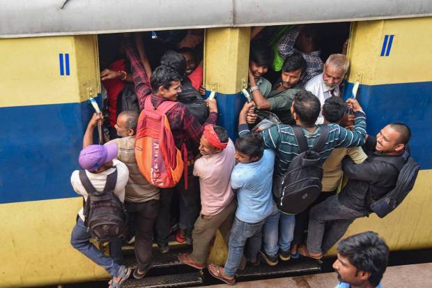Passengers hang from the doors of an overcrowded train as they travel home for the 'Chhath Puja' festival, at a railway station in Patna. (PTI Photo)
