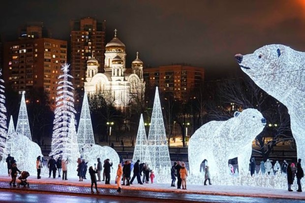 People walk and play at a park decorated for the New Year and Christmas festivities with an Orthodox Church in the background in Moscow on December 24. (AP)