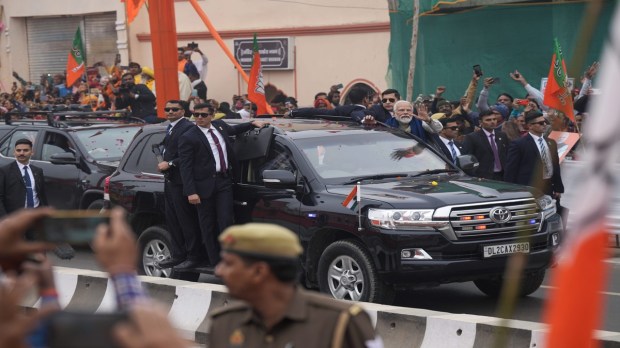 Prime Minister Narendra Modi greets the crowd of Ayodhya with a wave during a roadshow preceding the inauguration of a revamped station and a newly constructed airport. (Image: PTI)
