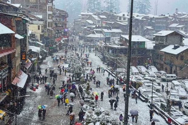 People walk under umbrellas on the Mall Road during snowfall, in Manali. (PTI Photo)