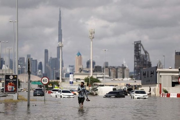 A person walks in flood water caused by heavy rains, with the Burj Khalifa tower visible in the background