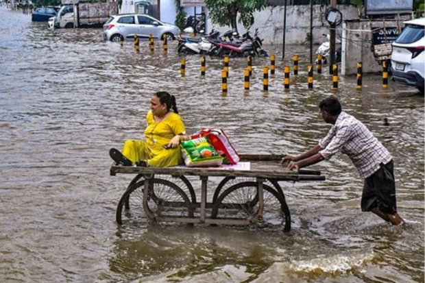 In Vadodara, a labourer pushes a cart carrying a woman to assist her in crossing a flooded road following a period of intense monsoon rainfall. (PTI Photo)