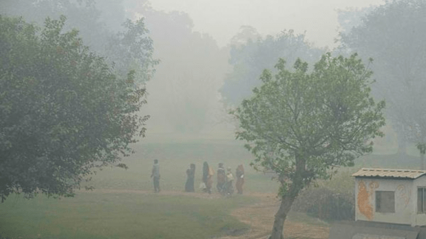 Labourers walk through a park amid low visibility caused by smog as air quality remains poor. (PTI)
