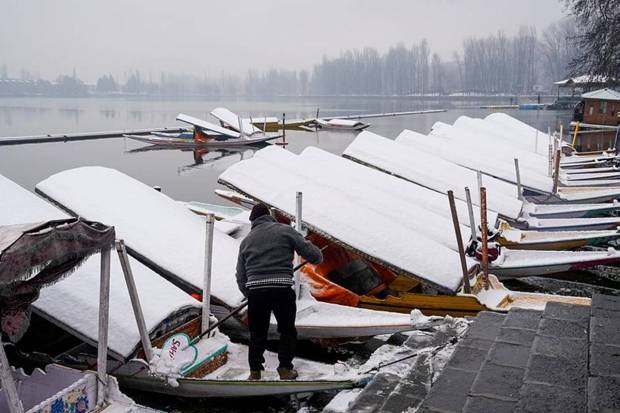 A boatman clears snow from his 'shikara' after fresh snowfall, at Dal Lake, in Srinagar. (Photo source: PTI)