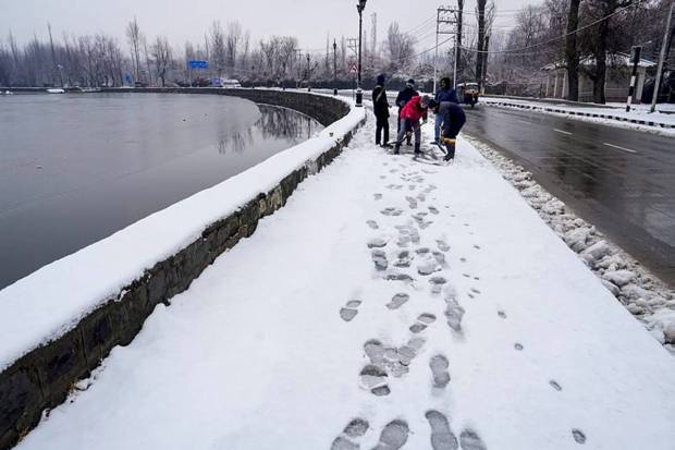 Workers clear snow from a pathway along Dal Lake after fresh snowfall, in Srinagar. (Photo source: PTI)