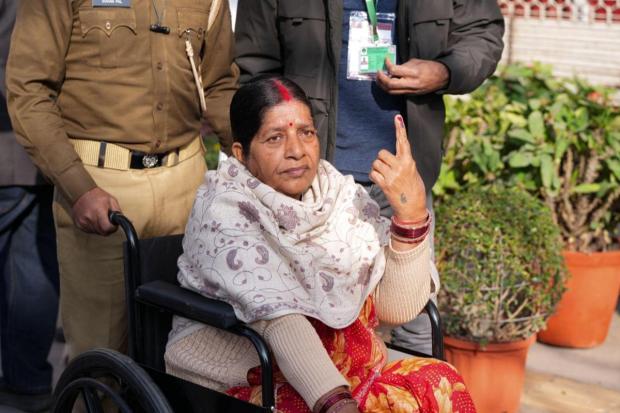 Disabled voter Rajkumari shows her inked finger after casting her vote at a polling booth during the Delhi Assembly elections.