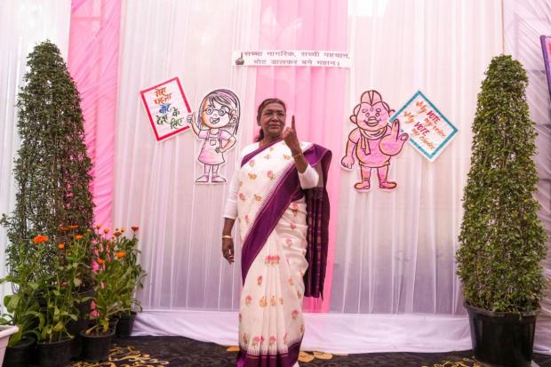 President Droupadi Murmu shows her finger marked with indelible ink after casting her vote at a polling booth during the Delhi Assembly elections.