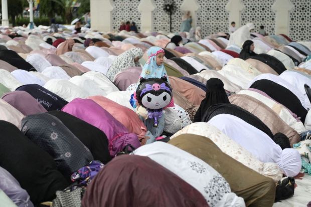 A girl attends Eid-al-Fitr prayers at the Baiturrahman mosque in  Banda Aceh, Indonesia. She plays with a balloon brining a spirit of innocence to the celebrations. (Image: Reuters)