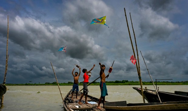 Boys fly kites as dark monsoon clouds fill the sky while standing on a boat on the River Hooghly in Nadia, West Bengal. (PTI Photo)