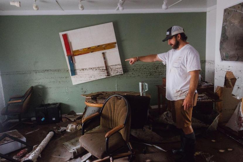 Man shows the damage to the office of his family's architectural business as a dirt line shows the extent of the flooding that the building faced.