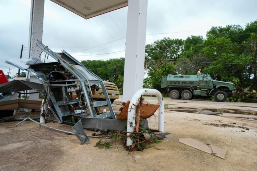 A Texas State Police armored vehicle rolls by a damaged gas pump at a gas station along the Guadalupe River.
