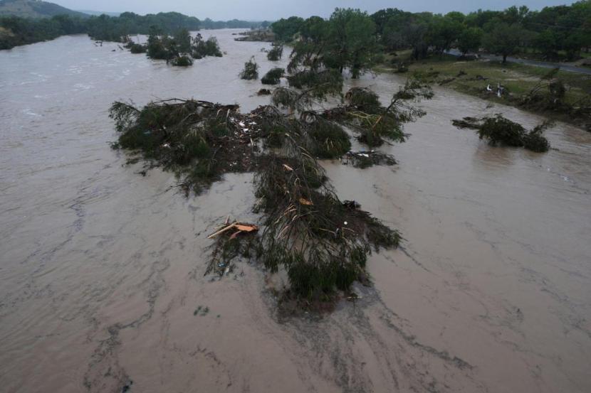 A raging Guadalupe River leaves fallen trees and debris in its wake.