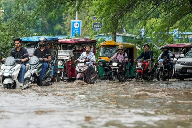 Commuters wade through a waterlogged road after rainfall, in New Delhi. (Photo source: PTI)