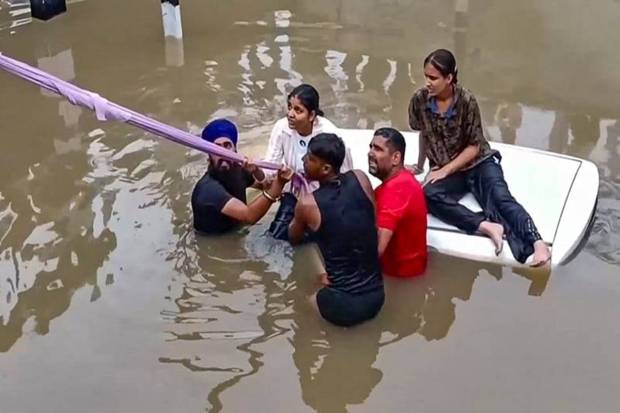 People rescue a family after a car got stuck at a waterlogged road under a bridge after heavy rainfall, in Moga, Punjab. (Photo source: PTI)