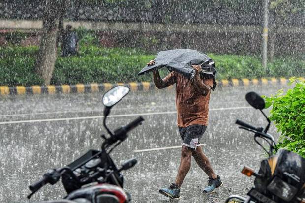A man covering his head with a plastic sheet, walks on a road amid heavy rainfall in the national capital. (Photo source: PTI)