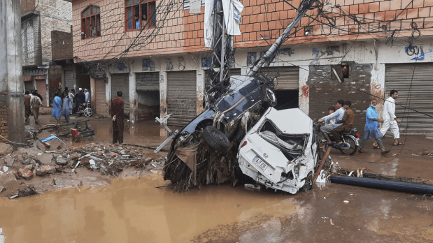 Residents walk next to damaged cars stuck to an electric pole following flash flooding due to heavy rains in a neighbourhood of Mingora, the main town of Swat Valley, northwestern Pakistan. (Photo Source: Associated Press)
