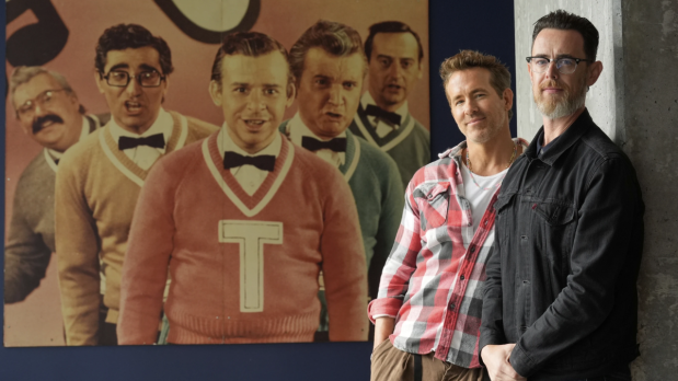 Colin Hanks (right), director, poses confidently with producer Ryan Reynolds (left) before a Second City cast photo, honoring comedy legend John Candy at TIFF.